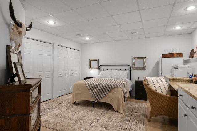 bedroom with a drop ceiling, light tile patterned flooring, and two closets