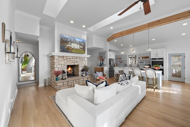 living room featuring a stone fireplace, vaulted ceiling with beams, ceiling fan, light wood-type flooring, and ornamental molding