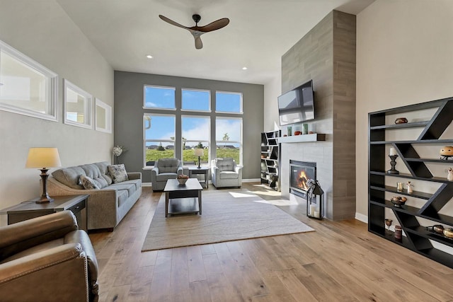 living room featuring a tiled fireplace, ceiling fan, and light wood-type flooring