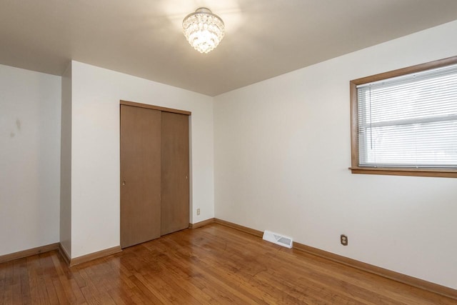 unfurnished bedroom with wood-type flooring, a closet, and a notable chandelier