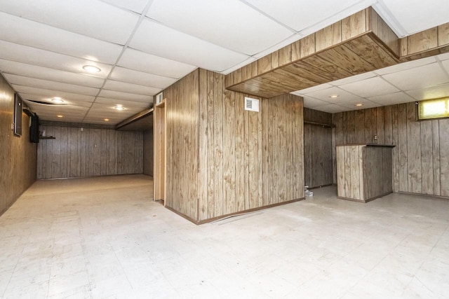 basement featuring a paneled ceiling and wood walls