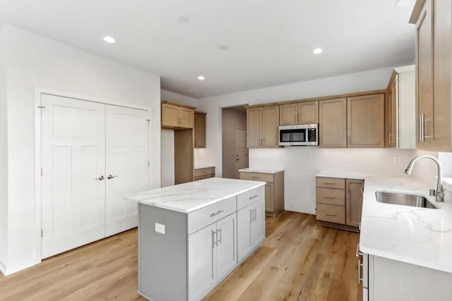 kitchen featuring a kitchen island, light stone countertops, sink, and light hardwood / wood-style flooring