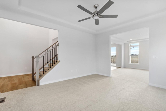 interior space with ceiling fan, a raised ceiling, and light carpet