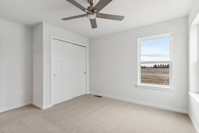 unfurnished bedroom featuring ceiling fan, light colored carpet, and a closet