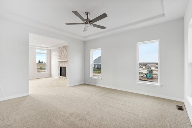 unfurnished living room featuring ceiling fan, a raised ceiling, light carpet, and a brick fireplace