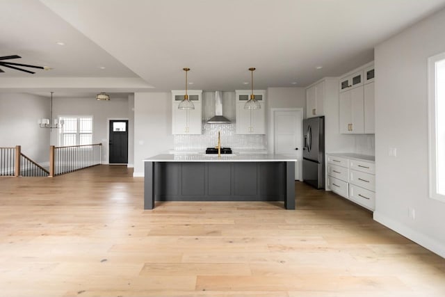 kitchen with pendant lighting, white cabinets, a center island with sink, wall chimney exhaust hood, and stainless steel fridge with ice dispenser