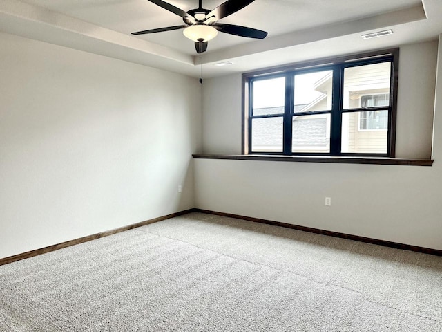 carpeted spare room with a tray ceiling and ceiling fan