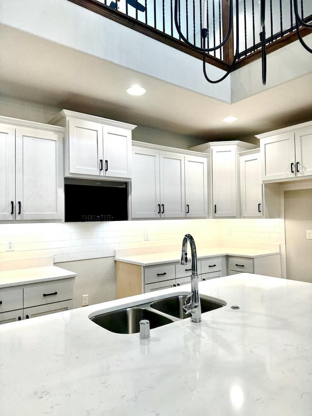 kitchen featuring light stone counters, white cabinetry, and sink