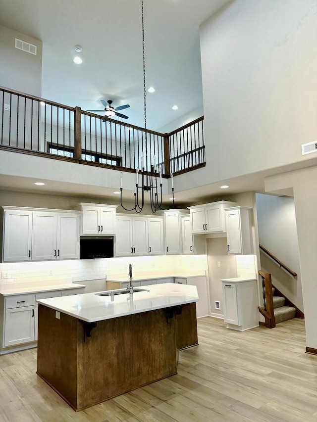 kitchen featuring a kitchen island with sink, a high ceiling, sink, ceiling fan, and white cabinetry