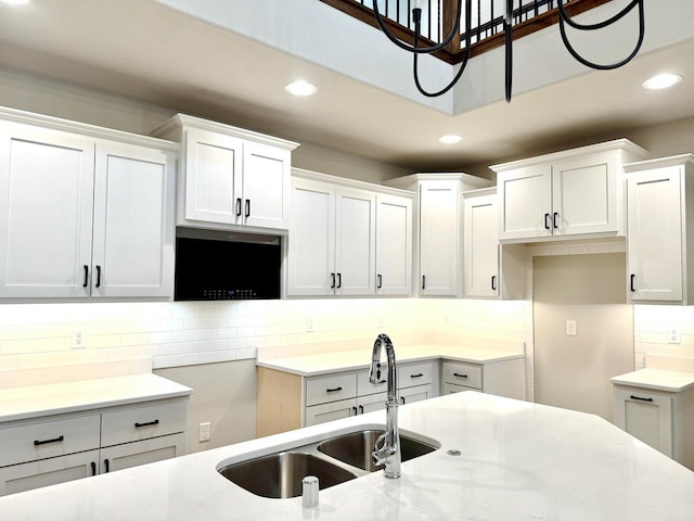 kitchen featuring backsplash, light stone countertops, sink, and white cabinets