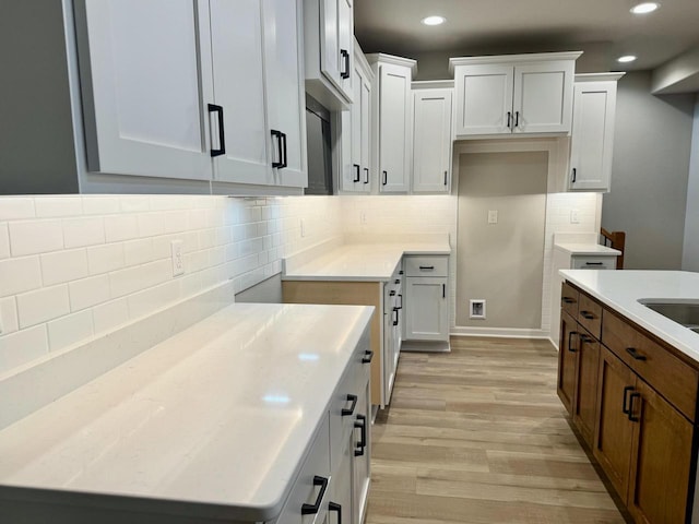 kitchen with tasteful backsplash, light stone countertops, white cabinets, and light hardwood / wood-style floors