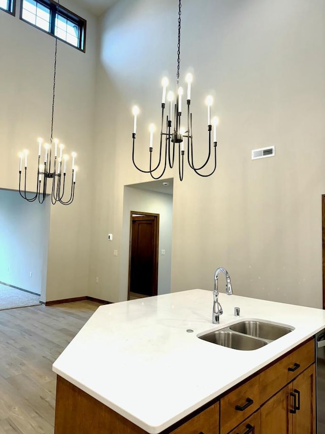 kitchen with a kitchen island with sink, sink, a towering ceiling, decorative light fixtures, and light hardwood / wood-style floors