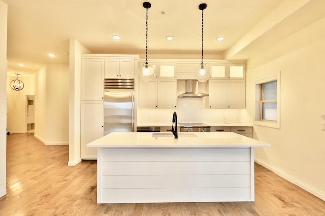 kitchen featuring a center island with sink, wall chimney exhaust hood, stainless steel built in refrigerator, and sink