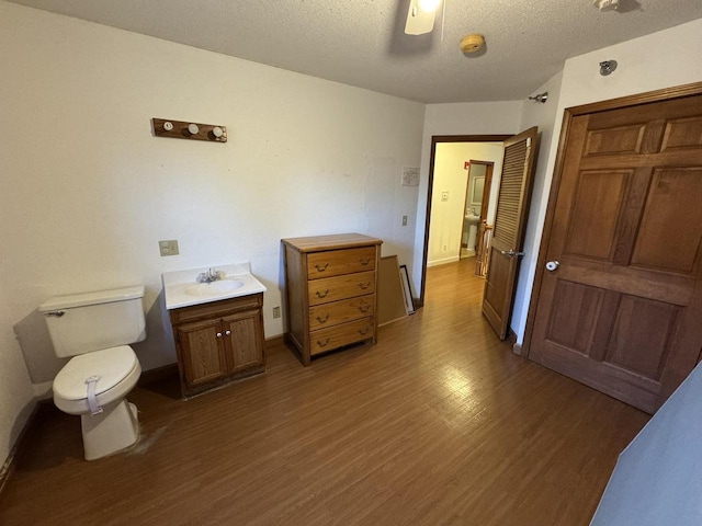 bathroom with hardwood / wood-style flooring, ceiling fan, vanity, a textured ceiling, and toilet