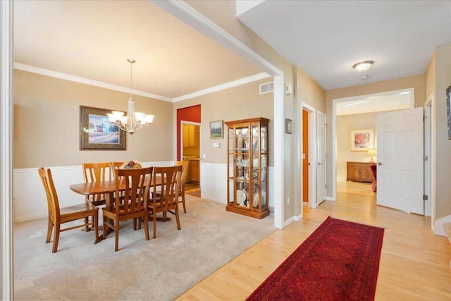 dining space with light wood-type flooring, crown molding, and an inviting chandelier