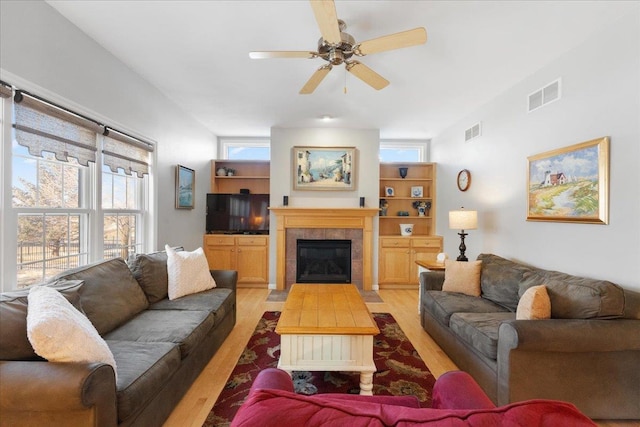 living room featuring a tile fireplace, ceiling fan, and light hardwood / wood-style flooring