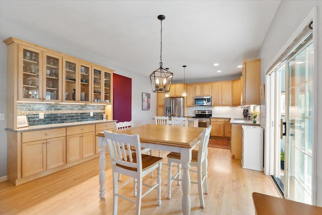 kitchen featuring decorative light fixtures, light brown cabinets, light hardwood / wood-style floors, tasteful backsplash, and appliances with stainless steel finishes