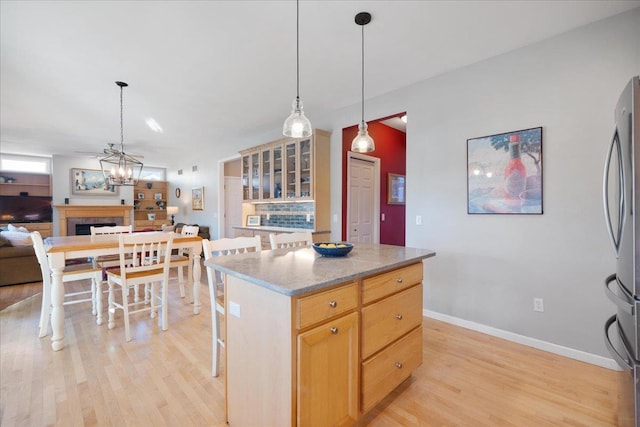 kitchen featuring light hardwood / wood-style floors, hanging light fixtures, a center island, stainless steel fridge, and a kitchen bar