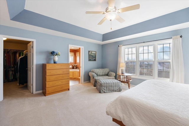 carpeted bedroom with ensuite bath, a spacious closet, a closet, a tray ceiling, and ceiling fan