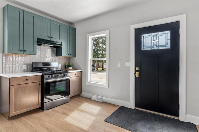 kitchen featuring stainless steel gas range oven, decorative backsplash, green cabinets, and light wood-type flooring