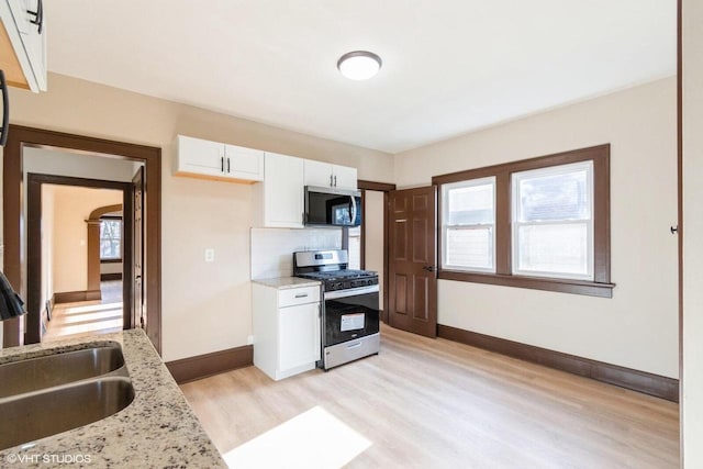 kitchen featuring light hardwood / wood-style flooring, light stone counters, white cabinetry, and stainless steel gas range