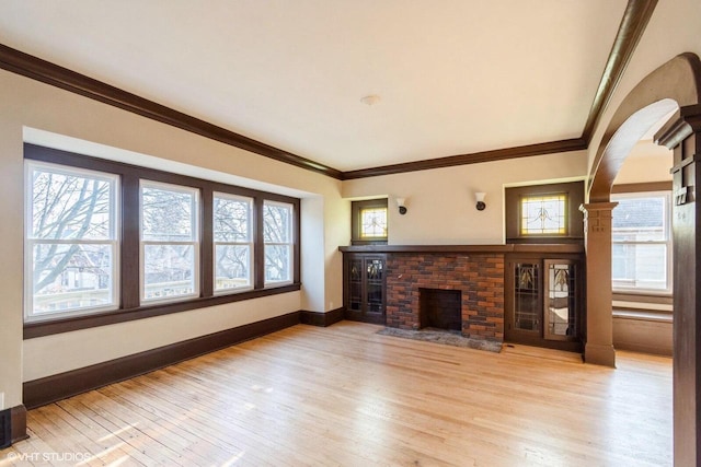 unfurnished living room with light wood-type flooring, a brick fireplace, and a healthy amount of sunlight