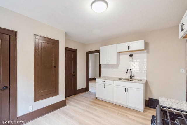 kitchen featuring sink, tasteful backsplash, light stone counters, light hardwood / wood-style flooring, and white cabinets