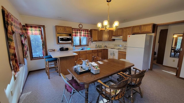 kitchen featuring white appliances, sink, pendant lighting, a notable chandelier, and a breakfast bar area