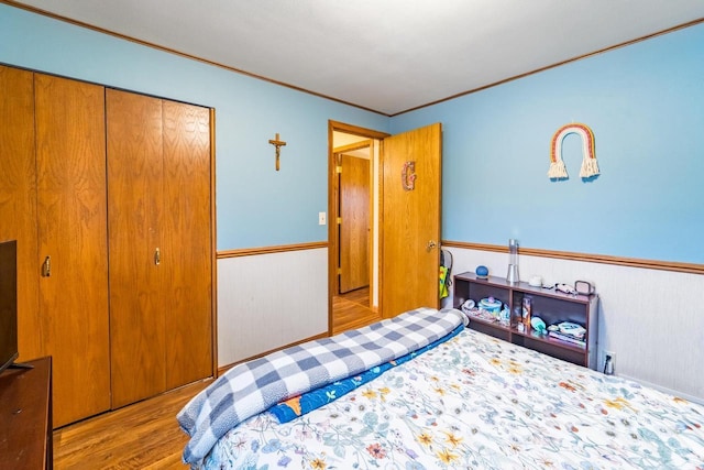 bedroom featuring light wood-type flooring, wooden walls, a closet, and crown molding