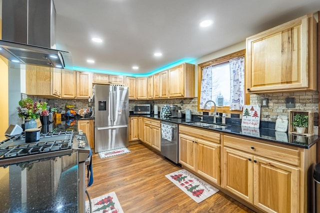 kitchen with appliances with stainless steel finishes, light wood-type flooring, dark stone counters, wall chimney exhaust hood, and sink