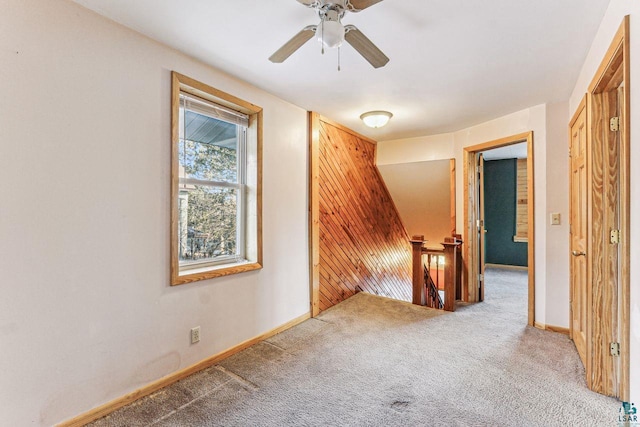 carpeted spare room with ceiling fan and wood walls