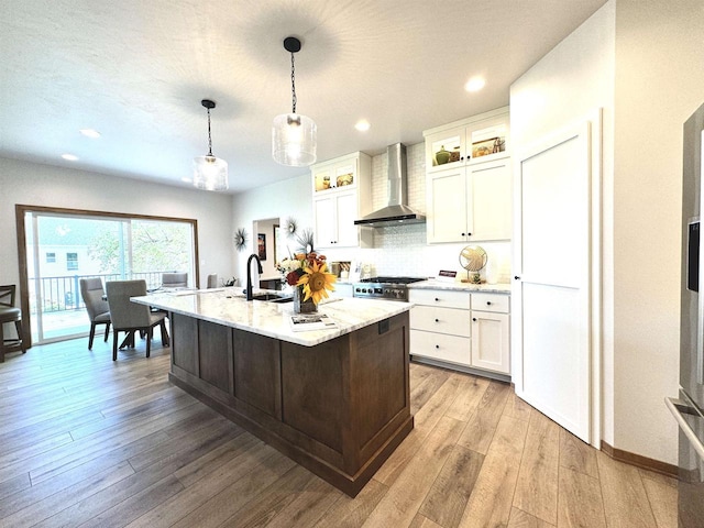 1217 Bay Mist Dr, Green Bay, WI 54311 - kitchen featuring wood-type flooring, wall chimney range hood, an island with sink, decorative light fixtures, and white cabinetry