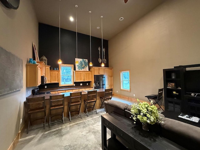 kitchen with hanging light fixtures, a high ceiling, black fridge with ice dispenser, decorative backsplash, and light brown cabinetry