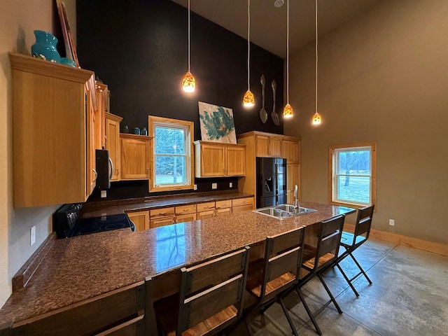 kitchen featuring light brown cabinetry, sink, black appliances, pendant lighting, and a high ceiling