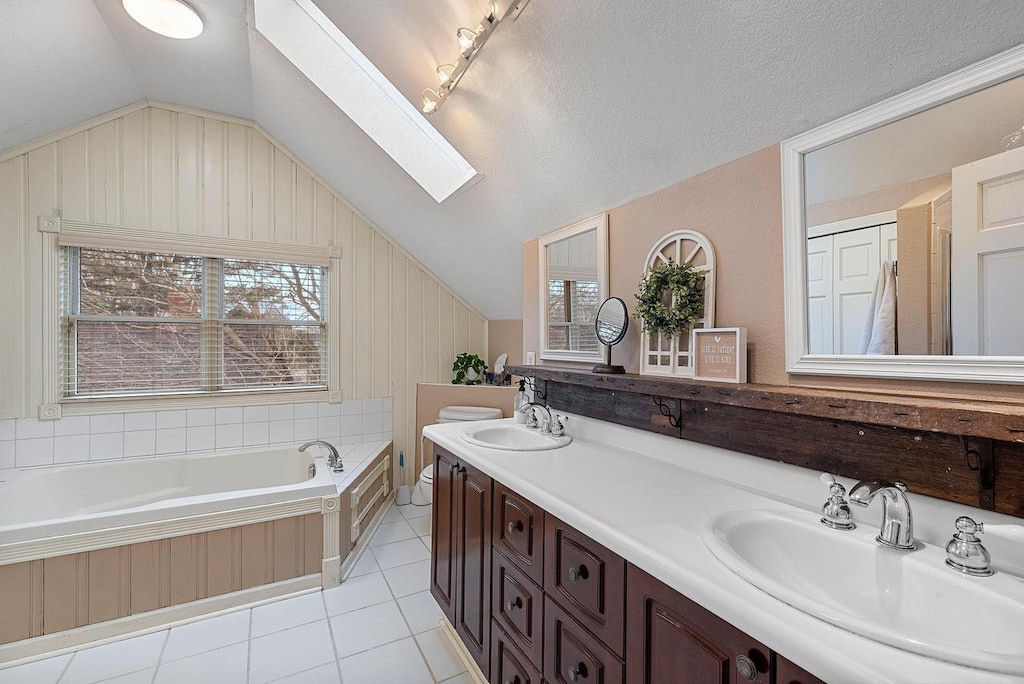 bathroom featuring a tub to relax in, a textured ceiling, vanity, lofted ceiling with skylight, and tile patterned flooring