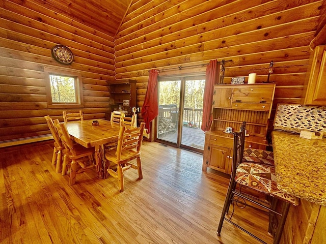 dining space with light hardwood / wood-style floors, rustic walls, and high vaulted ceiling