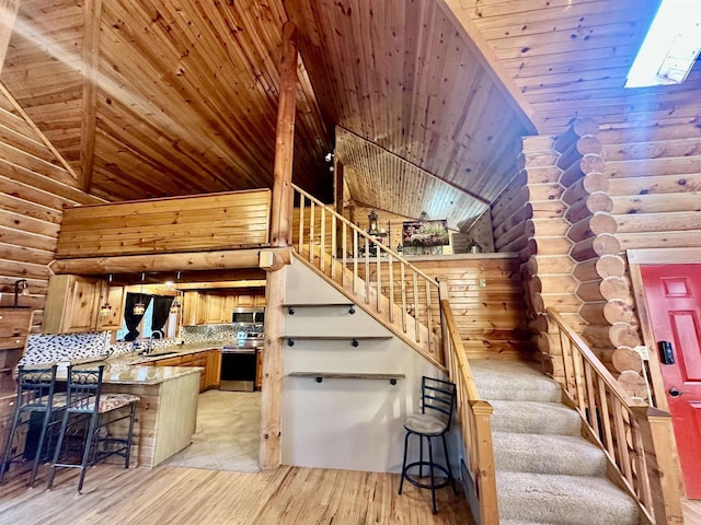 kitchen featuring a kitchen bar, wooden ceiling, stainless steel appliances, and log walls