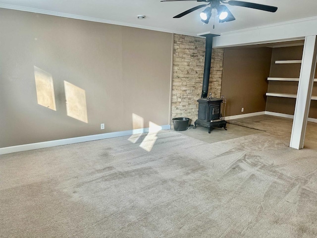 unfurnished living room featuring light colored carpet, a wood stove, ceiling fan, and crown molding