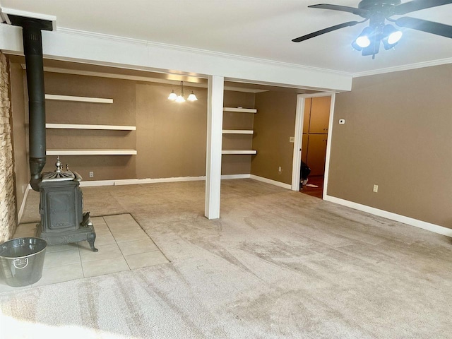 basement featuring carpet flooring, a wood stove, ceiling fan with notable chandelier, and ornamental molding