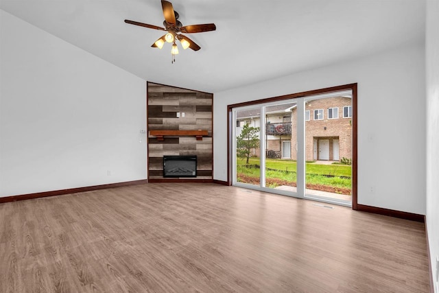 unfurnished living room with ceiling fan, a large fireplace, vaulted ceiling, and light hardwood / wood-style flooring