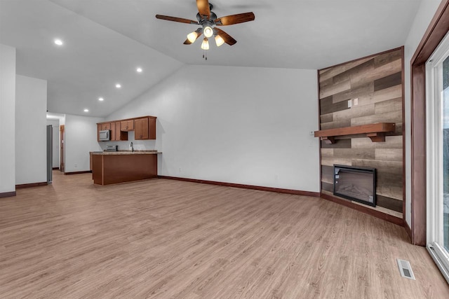 unfurnished living room with wood walls, vaulted ceiling, ceiling fan, a fireplace, and light hardwood / wood-style floors