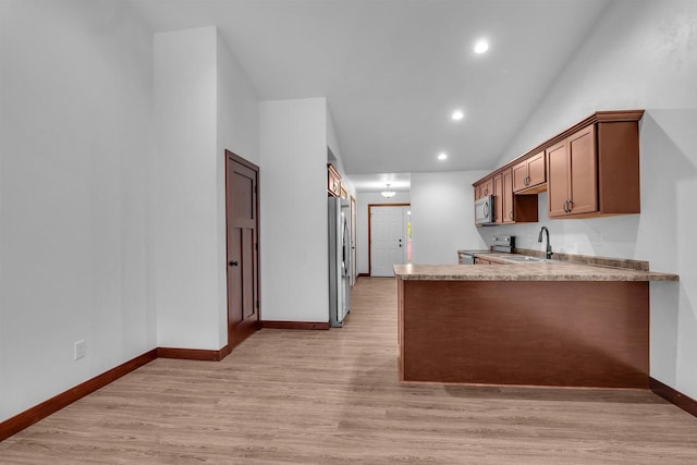 kitchen featuring stainless steel appliances, light stone counters, kitchen peninsula, lofted ceiling, and light wood-type flooring