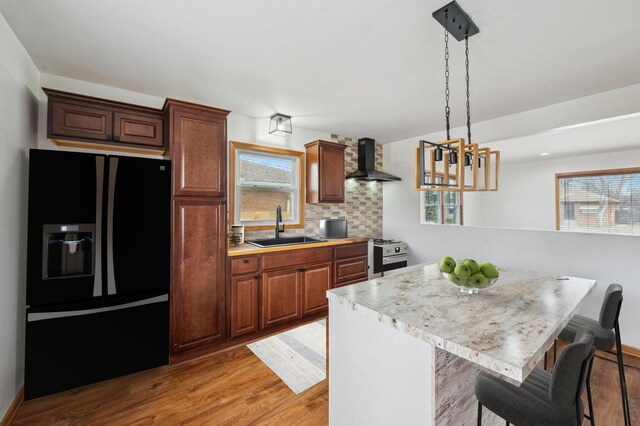 kitchen with sink, wall chimney exhaust hood, black fridge, a breakfast bar area, and decorative backsplash