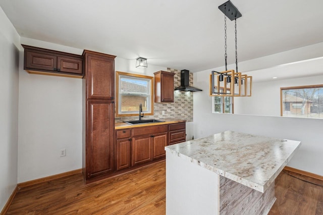 kitchen with tasteful backsplash, a wealth of natural light, wall chimney exhaust hood, sink, and hanging light fixtures