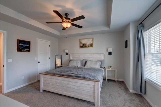 bedroom with ceiling fan, multiple windows, light carpet, and a tray ceiling