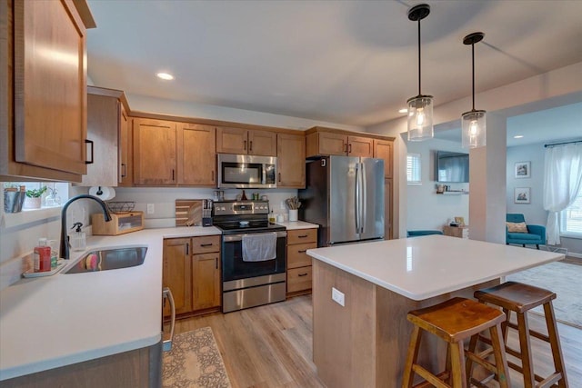 kitchen with sink, a wealth of natural light, appliances with stainless steel finishes, decorative light fixtures, and light hardwood / wood-style floors