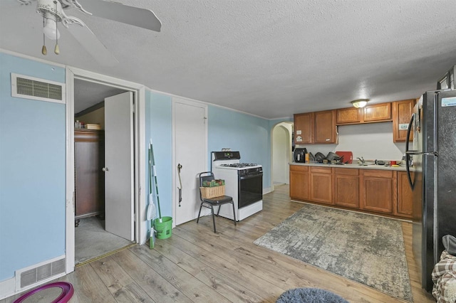 kitchen with sink, light hardwood / wood-style floors, a textured ceiling, black refrigerator, and white gas range oven