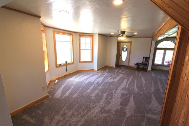 entryway with dark colored carpet, ornamental molding, ceiling fan, and a healthy amount of sunlight