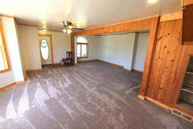 unfurnished living room featuring wood walls, ceiling fan, and dark colored carpet