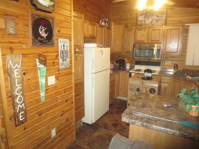 kitchen with light brown cabinetry, white appliances, wooden walls, and dark stone countertops